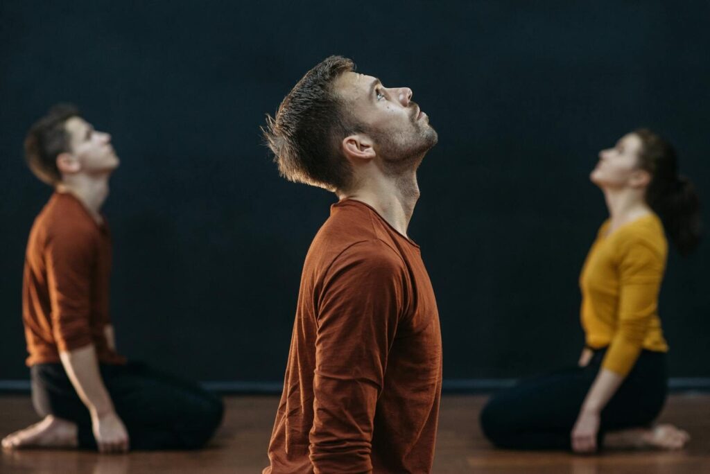 A group of three adults engaged in focused meditation looking upwards with intent expressions.